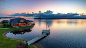 Serene waterfront home with dock at sunrise, calm lake water reflecting sky, professional landscaping, luxury real estate photography