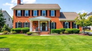 Beautiful suburban two-story colonial home with brick exterior, white trim, manicured lawn, flowering landscaping, and welcoming front porch in Maryland neighborhood